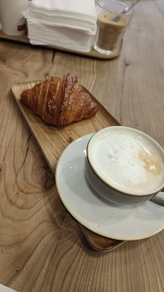 Un croissant et un cappuccino posés sur la grande table en bois de la boutique