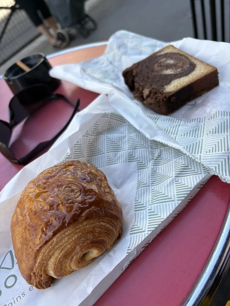 Un pain au chocolat et une part de cake marbré emballés, sur une table devant la boutique